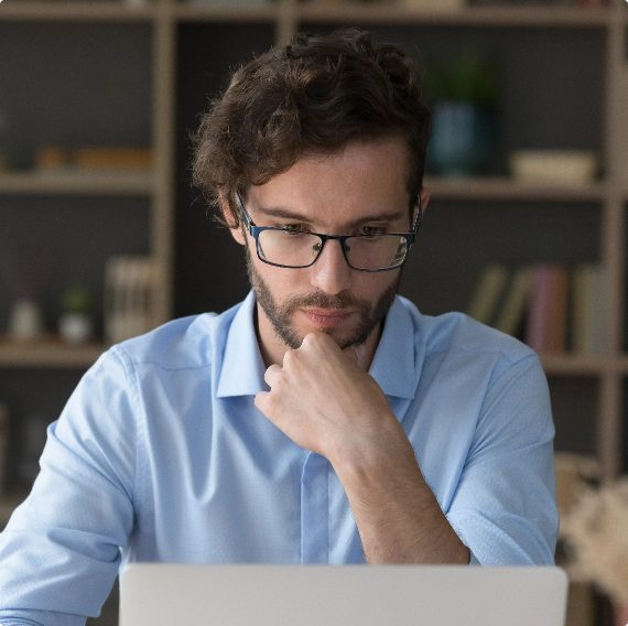 Man in blue shirt and eyeglasses staring at laptop screen