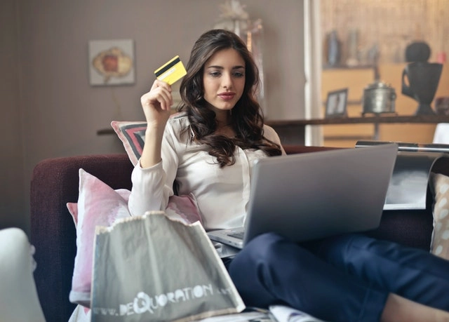 A woman holds a credit card while shopping online.