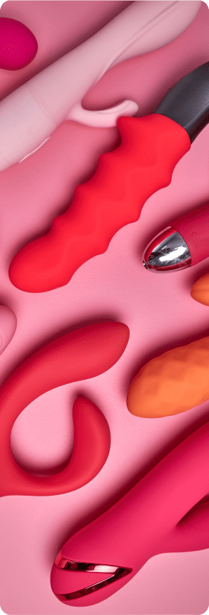 A flat lay composition of multiple vibrators and adult toys in vibrant shades of pink, red, and orange arranged on a solid pink background.