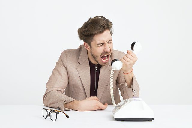 an angry man in a brown blazer yelling into a phone