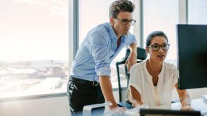 Two marketing professionals reviewing Google Ads automation performance on a desktop monitor in a bright office.