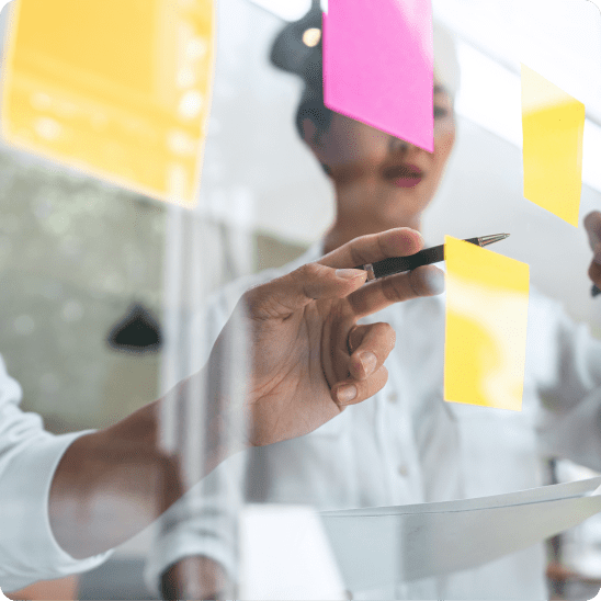 Person writing on a glass board with yellow and pink sticky notes for ChatGPT ads strategy in a bright office setting.