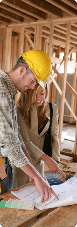 Construction professional and client review plans and color samples inside a framed building.