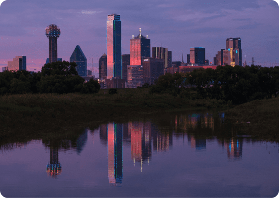 A purple-tinted Dallas skyline and its reflection in water at twilight