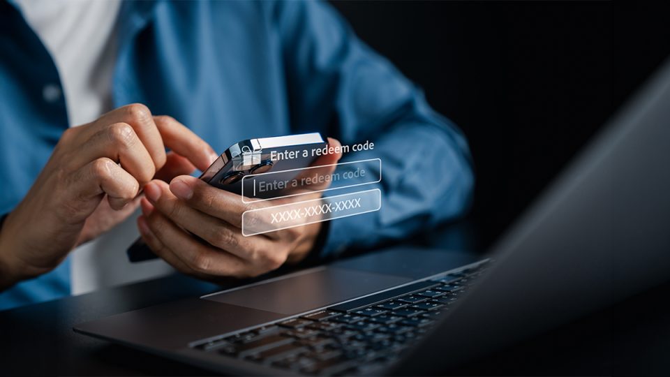 Person entering a gift card redeem code on a smartphone beside a laptop.