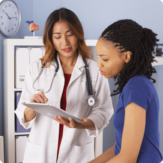 Doctor showing information on a tablet to a patient in a clinical office, both looking at the screen during an in-person consultation