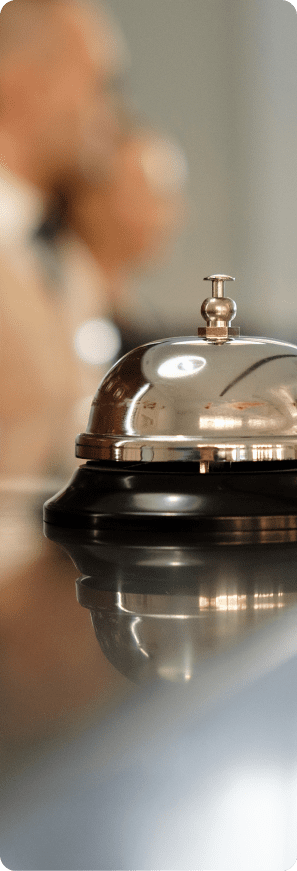 Service bell on a hotel reception desk with guests blurred in the background.