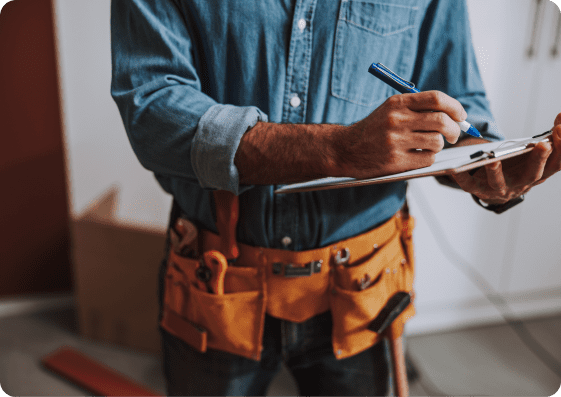 Home services professional wearing a tool belt and writing notes on a clipboard during an in-home service visit.