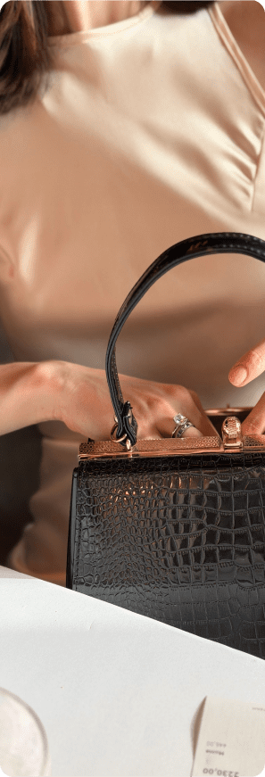 Woman opening a black luxury handbag while wearing jewelry at a table.