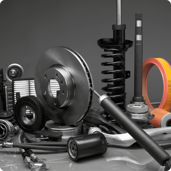 Automotive parts, including brake rotors, filters, shocks, and suspension components, arranged on a studio surface.