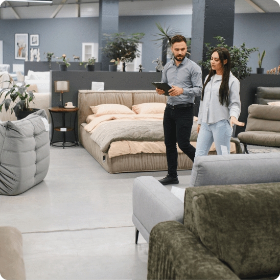 Sales associate assists a customer browsing sofas and home furnishings in a furniture showroom.