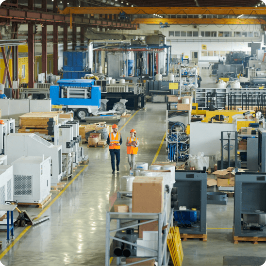 Industrial workers walk through a large manufacturing facility filled with machinery and equipment.