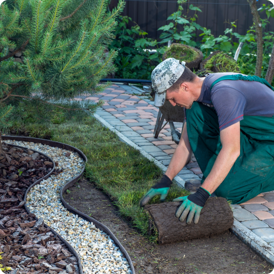 Landscaper lays grass along a garden path in a residential yard.