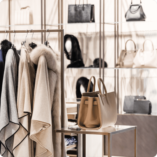 Luxury boutique display with coats, handbags, and accessories arranged on racks and shelves.