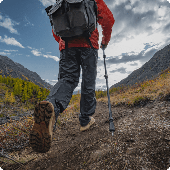 Hiker with a backpack and trekking pole walks through a mountain trail.