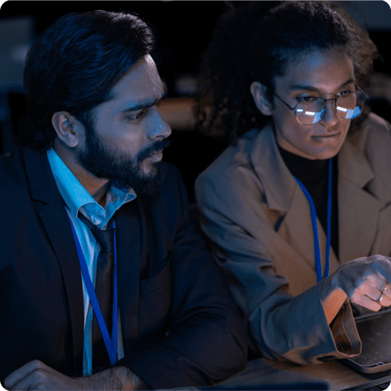 Software professionals review data together on a computer in a dark office setting.