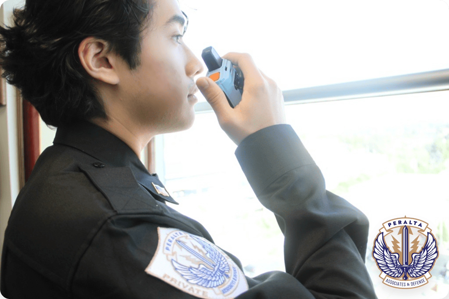 A private security guard in a black uniform looking out a window while holding a light blue two-way radio up to his face. The uniform patch and an overlay in the bottom right corner display the "Peralta Associates & Defense" logo.