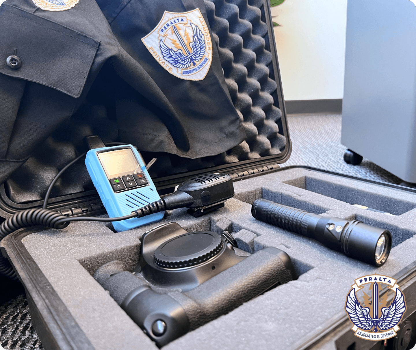 An open, foam-lined tactical gear case containing surveillance and security equipment, including a light blue radio with a shoulder mic, a black flashlight, and a DSLR camera body. A black uniform shirt draped over the lid features the "Peralta Security" patch.