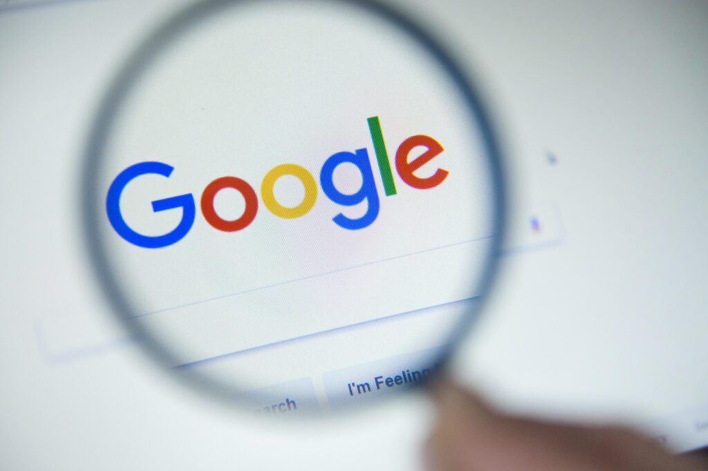 A person holding a magnifying glass to the Google search bar.