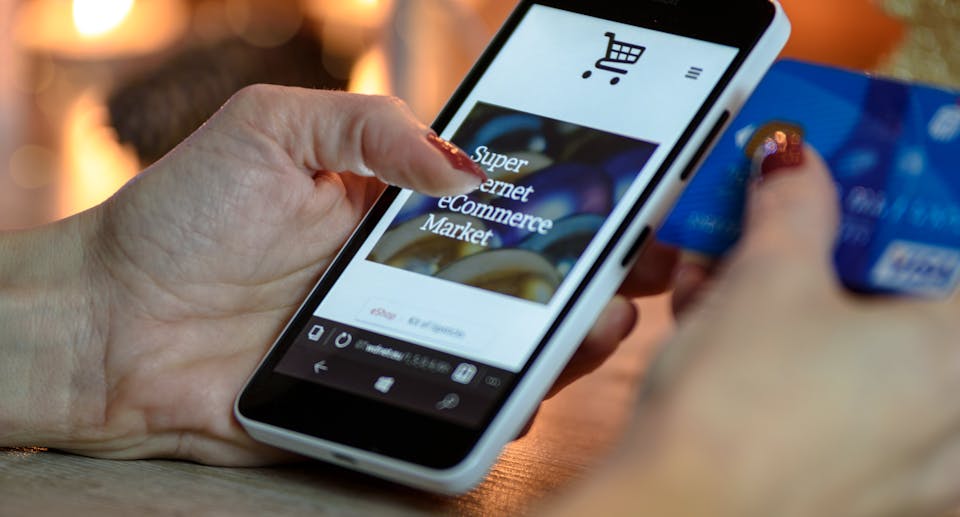 Person Using Smartphone to Shop Online While Holding Blue Credit Card