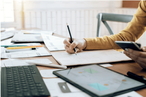 a person writing in a notebook on a cluttered desk