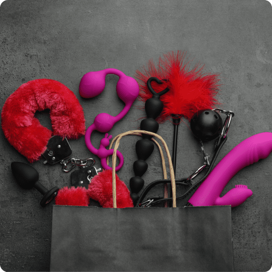 A grey shopping bag lying on its side on a dark grey surface, with an assortment of adult toys spilling out of it.