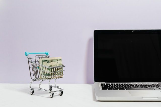 a shopping cart containing money next to a laptop