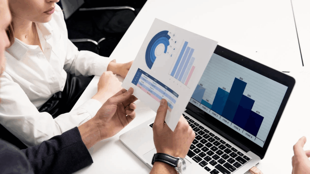 Two people looking at graphs and charts on paper and on a laptop